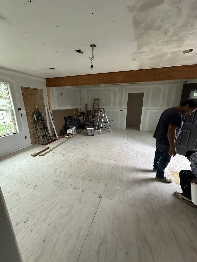 Open living and kitchen space with new drywall, a wood beam across the ceiling and the subfloor down.