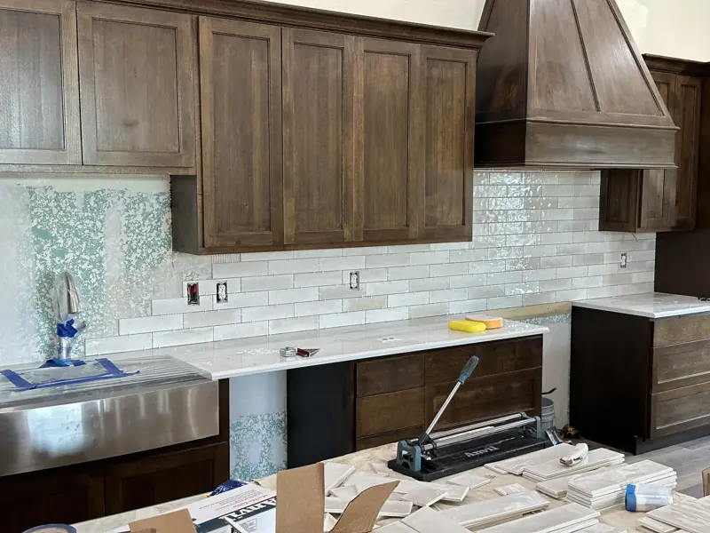 Kitchen with dark stained cabinets and range hood, a white subway tile backsplash and white countertops.