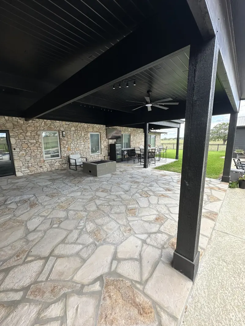 Flagstone patio under a black plank ceiling with track lights and fan, concrete fire pit and dining set by the house.