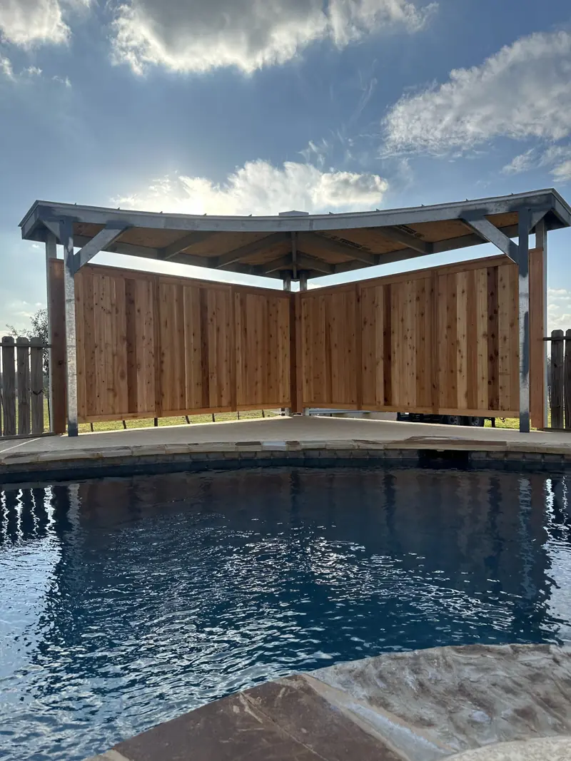 The rounded pool cover with its roof on and cedar walls, seen across the pool.