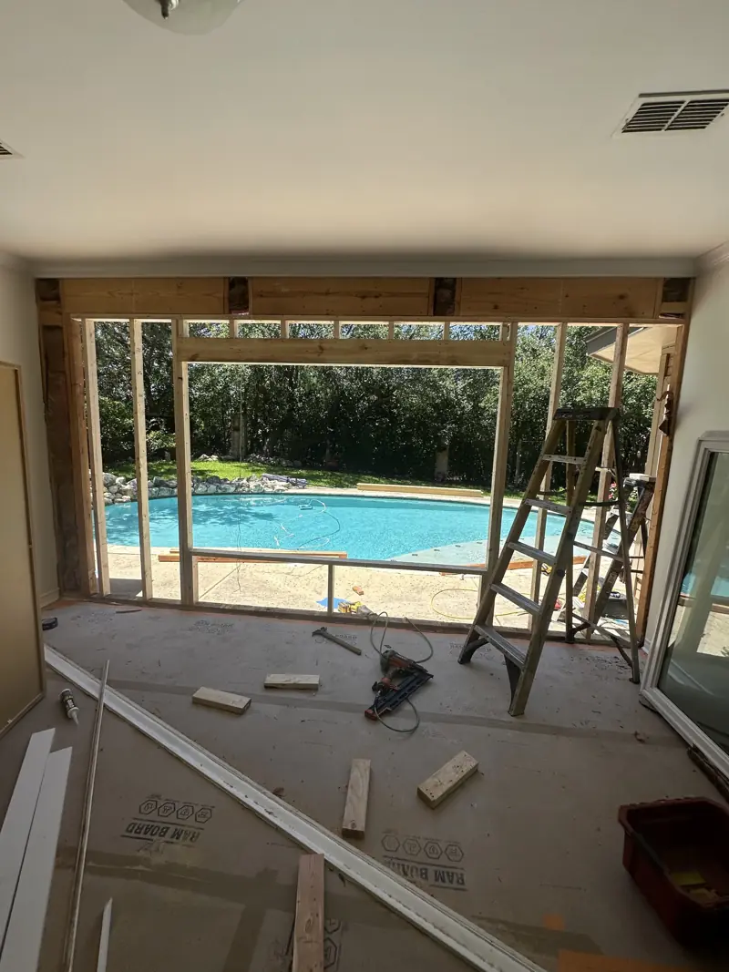 Wall opened and reframed for the new window, pool visible outside, floor covered in protection board.